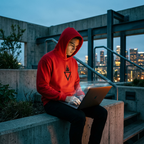 Junger Mann im roten PROMETHEUS Kapuzenpullover tippt auf Laptop mit Hologramm-Anzeige auf Dachterrasse nachts.